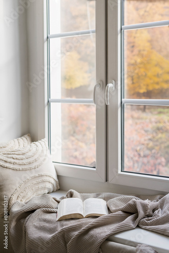 Fotografía Cozy sitting place on window sill with cushions, soft plaid and open book