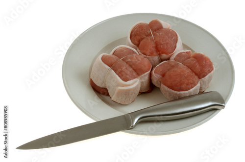 Trois paupiettes de veau crues dans une assiette avec un couteau en gros plan sur fond blanc