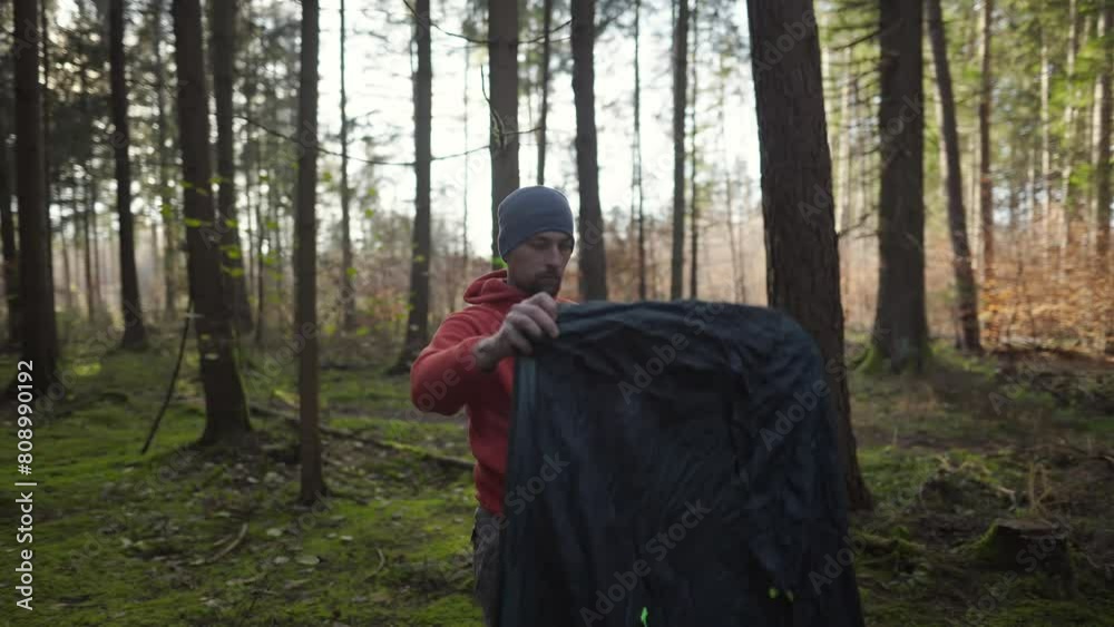 Tourist makes camp in woods, sets up tent in meadow in fall forest, prepares for an overnight stay in campsite. Backpacker builds tent on solo autumn trip in forest. Hiking and staying in nature. Tourist makes camp in woods, sets up tent in meadow in fall forest, prepares for an overnight stay in campsite. Backpacker builds tent on solo autumn trip in forest. Hiking and staying in nature.