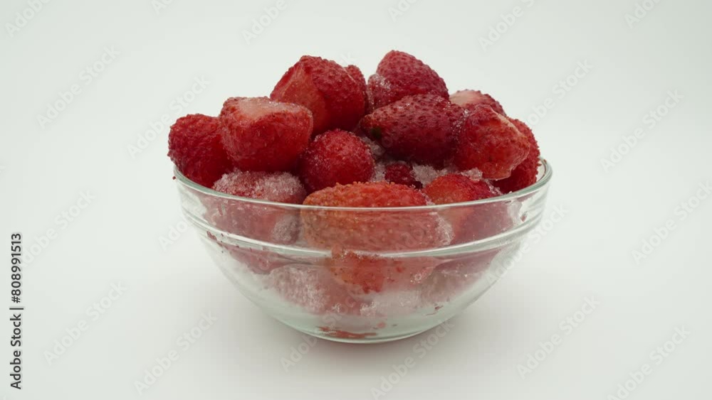 Time-lapse of frozen steam less strawberries thawing in clear glass round container against white background. Video can be reversed to achieve freezing like effect.