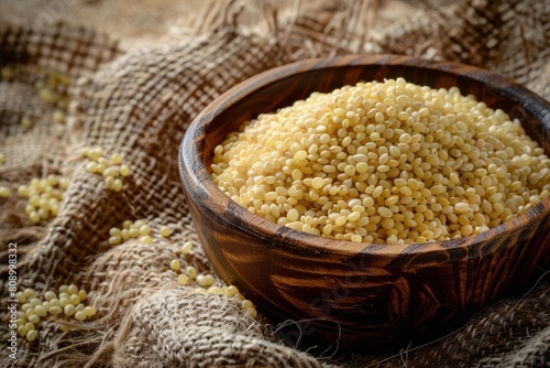 raw organic millet groats in rustic wooden bowl on textured burlap background food photography