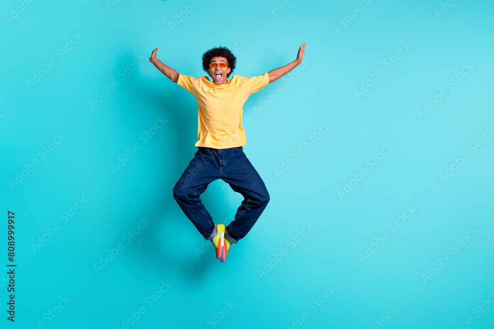 Full size photo of eccentric man wear oversize t-shirt denim pants in glasses jumping hands like wings isolated on teal color background