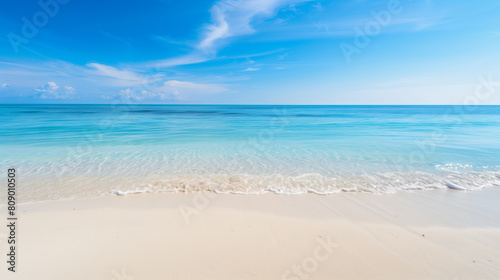 A beautiful beach with a clear blue ocean and a few small islands in the distance. The sky is mostly clear with a few clouds scattered throughout. The scene is peaceful and serene  with the calm ocean