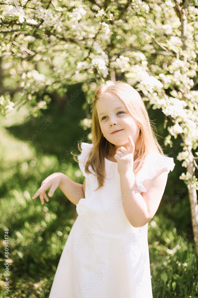 Portrait of little toddler girl in white romantic dress in blossoming garden in spring. Cute beautiful lovely child having fun in a park on a sunny day. Portrait of little toddler girl in white romantic dress in blossoming garden in spring. Cute beautiful lovely child having fun in a park on a sunny day.