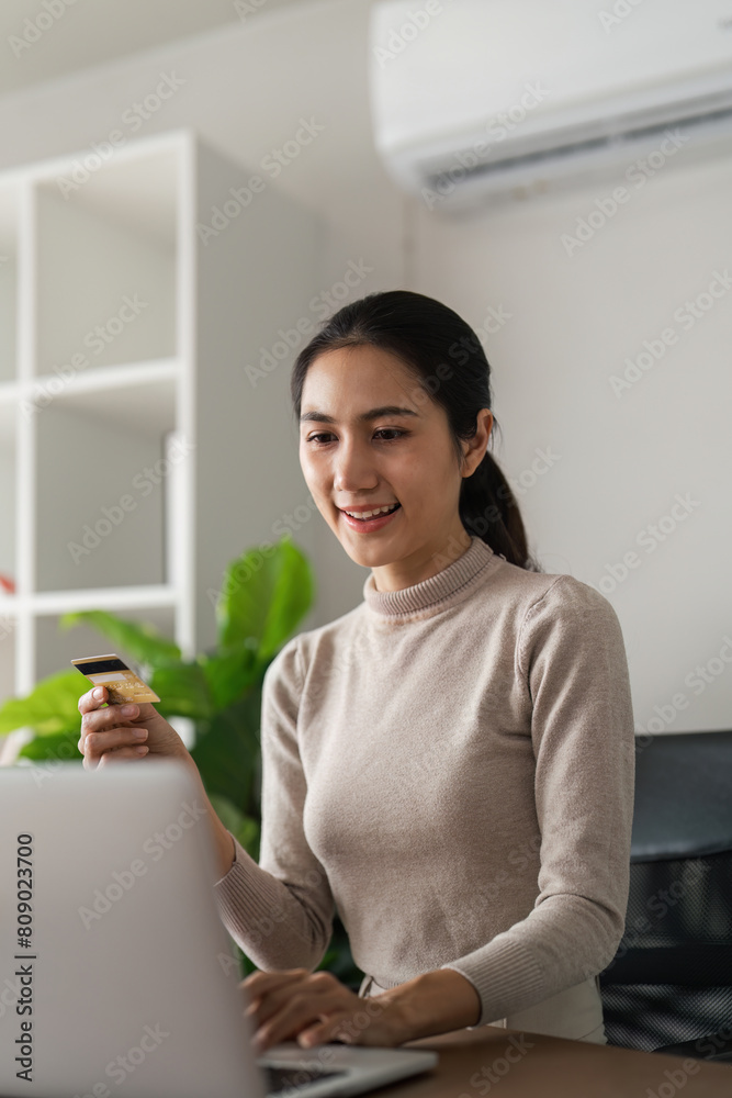 A woman is sitting at a desk with a laptop and a credit card in her hand
