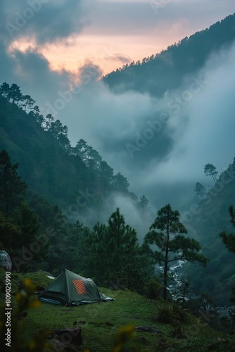 Tent on a hillside with a dramatic view of misty mountains and a colorful sunrise in the background