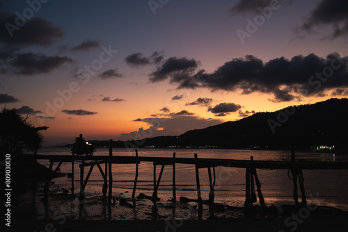 sunset over the ocean with wood bridge with a motorbike driving over it in thailand koh samui