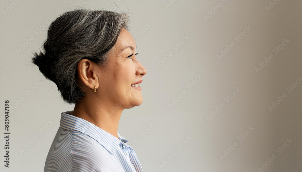 Side profile view head and shoulders of happy middle-aged woman staring straight posing alone against gray studio background with copy space. Services for elderly, optimism, midlife and wise quotes Side profile view head and shoulders of happy middle-aged woman staring straight posing alone against gray studio background with copy space. Services for elderly, optimism, midlife and wise quotes