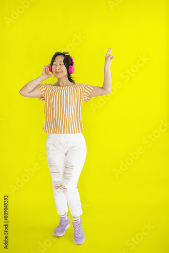 Full length body size photo of dancing Asian girl imagining herself at disco while isolated on yellow background.