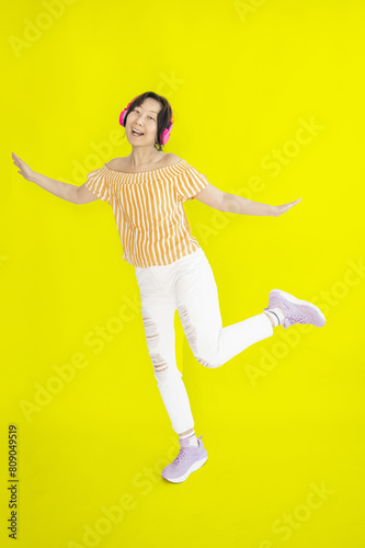 Full length body size photo of dancing Asian girl imagining herself at disco while isolated on yellow background.