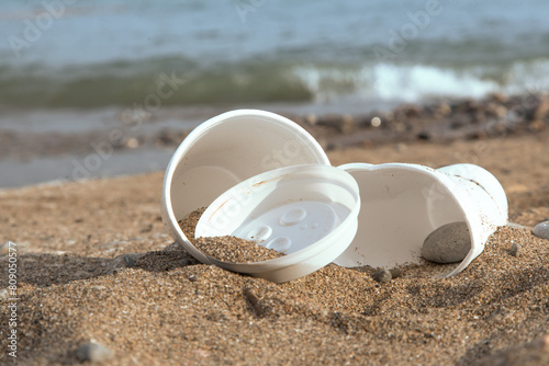 close up of garbage plastic coffee cups lying on a beach photo