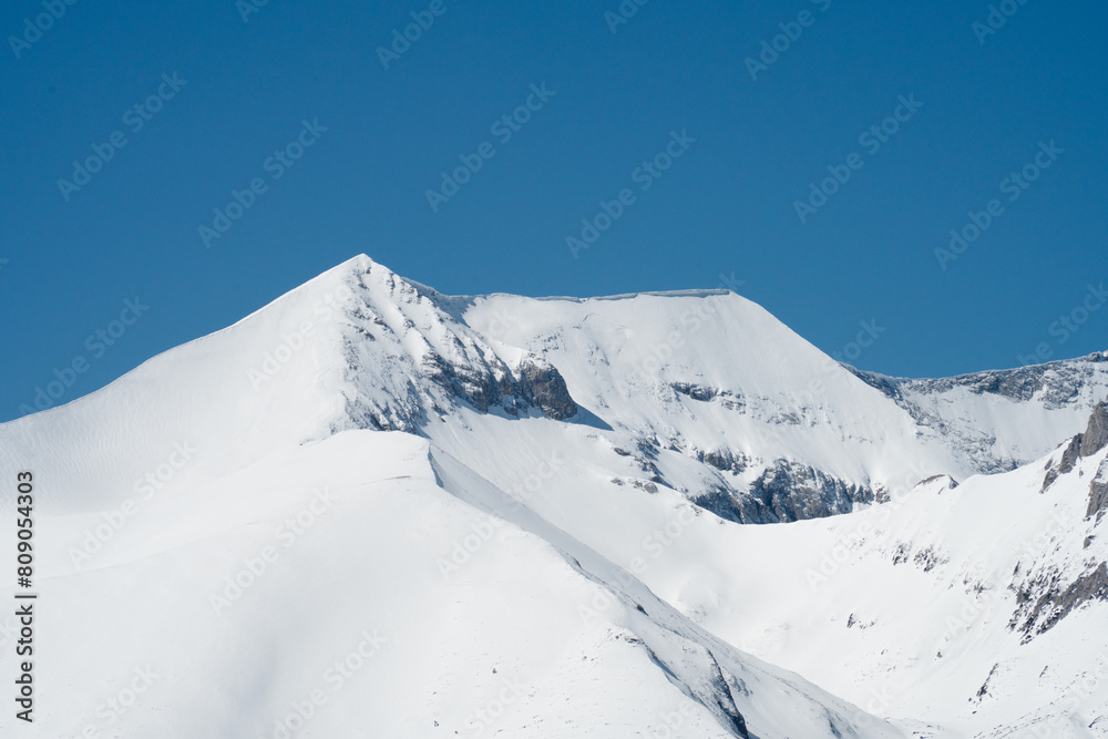 Peaks Kutelo 1 and 2 of the Pirin Mountains covered in snow were photographed from a distant slope with telephoto lens. Peaks Kutelo 1 and 2 of the Pirin Mountains covered in snow were photographed from a distant slope with telephoto lens.