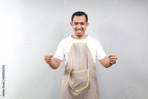 Friendly asian coffee shop waiter standing with raised hands clenched, standing over gray background photo