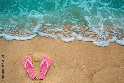 Pink flip flops on a beach sand near the turquoise sea. Sea with beautiful waves and transparent aqua blue water.