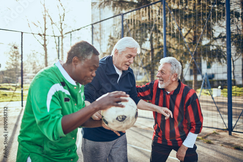 Senior men playing soccer and discussing strategy in urban park photo