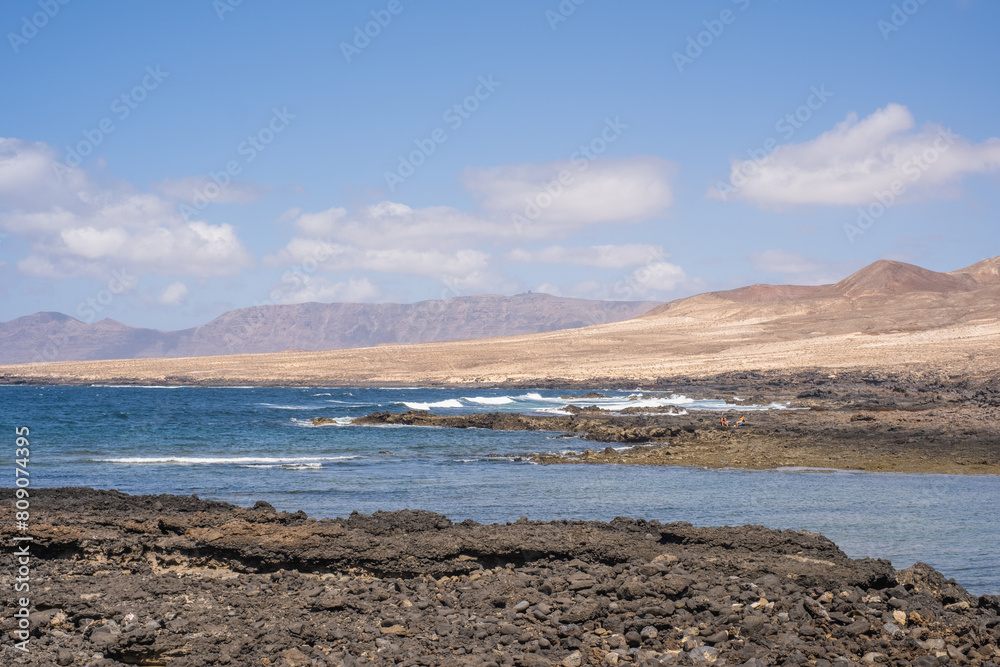 Bay and typical houses of the fishing village of Caleta de Caballo. White houses. Rock coast in the foreground. Turquoise water. Calm sea. Caleta de Caballo, Lanzarote, Canary Islands, Spain