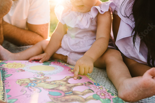 Read book baby. Young family relaxing on vacation together. Father, mother, little girl reading book on blanket in summer at sunset. Portrait mom, dad, daughter closeup. Concept of holiday on picnic