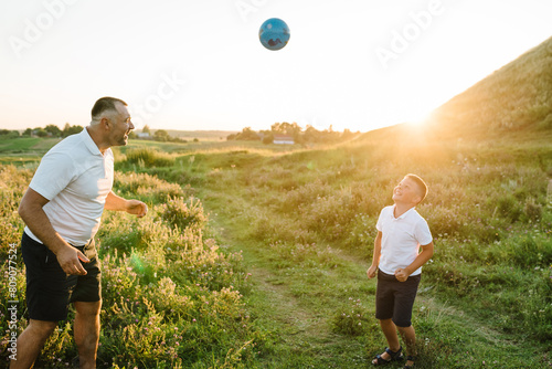 Father and young boy playing in field with soccer ball. Handsome dad with little cute son playing football on green grass at sunset. Concept of having fun and sport. Friendly family. Father's Day.