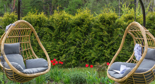 Rattan garden swing with cushion in the garden, seating area in the yard. Summer vacation concept