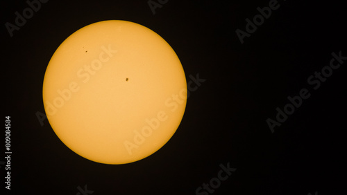 Color photo showing the full sun with a few visible sunspots against a black sky background with copy space.