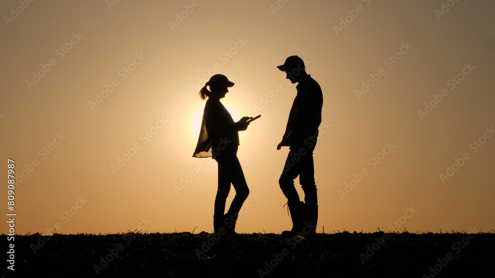 Silhouettes of two business people communicating outdoors, using a tablet