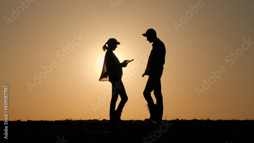 Silhouettes of two business people communicating outdoors, using a tablet