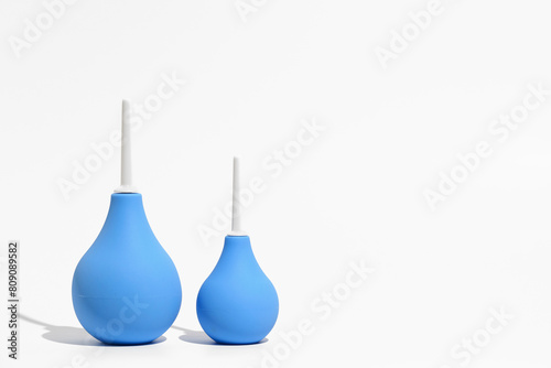 Two blue enemas - a larger and a smaller one on a white isolated background. Place for your text, design. The concept of pharmacy, medical drugs, bowel cleansing and body detoxification.