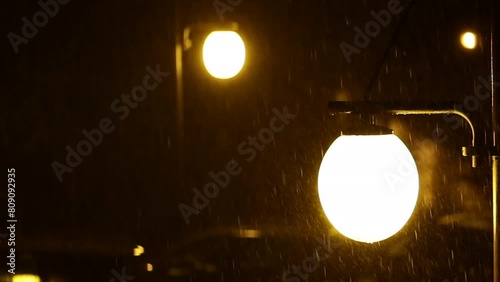 inquadratura particolare e rallentata che mostra due lampioni stradali di notte che emettono una luce gialla ed illuminano la pioggia che cade durante un temporale photo