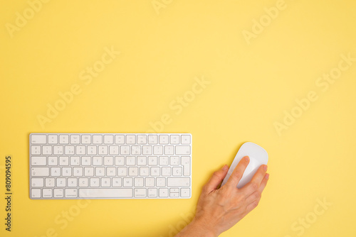 a person is using a computer keyboard with a mouse on a yellow background. Copy space