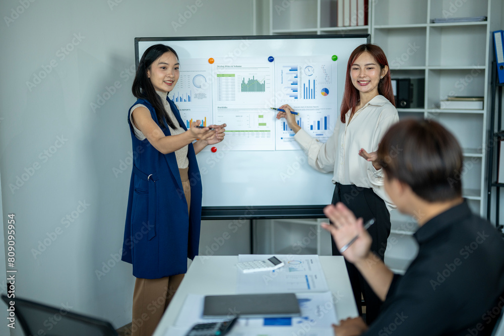 Three people are in a meeting room, with two women and a man. The women are presenting data on a whiteboard, while the man is listening. Scene is professional and focused Three people are in a meeting room, with two women and a man. The women are presenting data on a whiteboard, while the man is listening. Scene is professional and focused