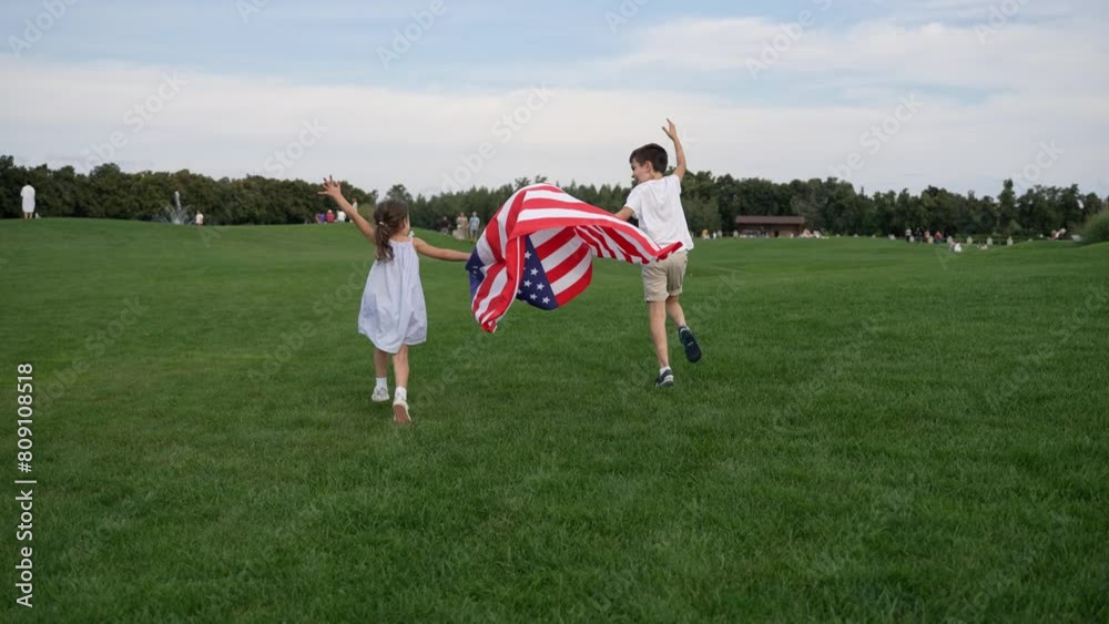 Mixed race boy and girl playing with American flag in a grassy field on 4th July under a clear sky, surrounded by trees. Happy and carefree kids enjoying the leisure outdoors. 4k High res Mixed race boy and girl playing with American flag in a grassy field on 4th July under a clear sky, surrounded by trees. Happy and carefree kids enjoying the leisure outdoors. 4k High res