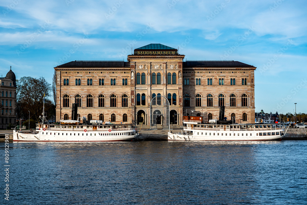 National Museum of Fine Arts (Nationalmuseum) building located on peninsula Blasieholmen in city centre with white boats, ships on Lake Malaren water, blue sky background, Stockholm, Sweden
