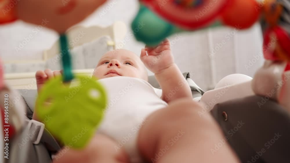 Newborn baby lies in cocoon chaise longue, infant is active, looking at multi-colored children toys hanging on baby chair bed. Chaise lounge for relaxation and development of child.