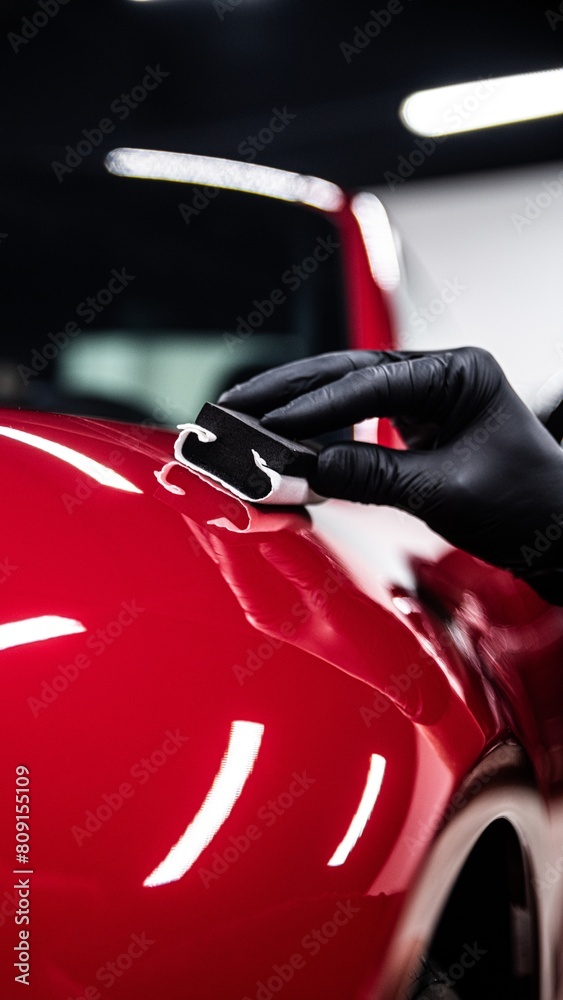 Car detailing studio worker carefully applying ceramic coating on red car