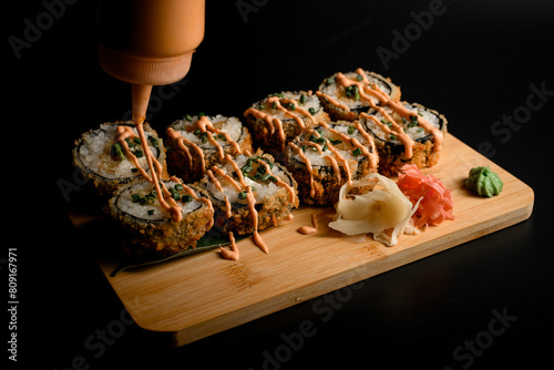 Tasty breaded sushi assortment on wooden board with sauce, ginger.