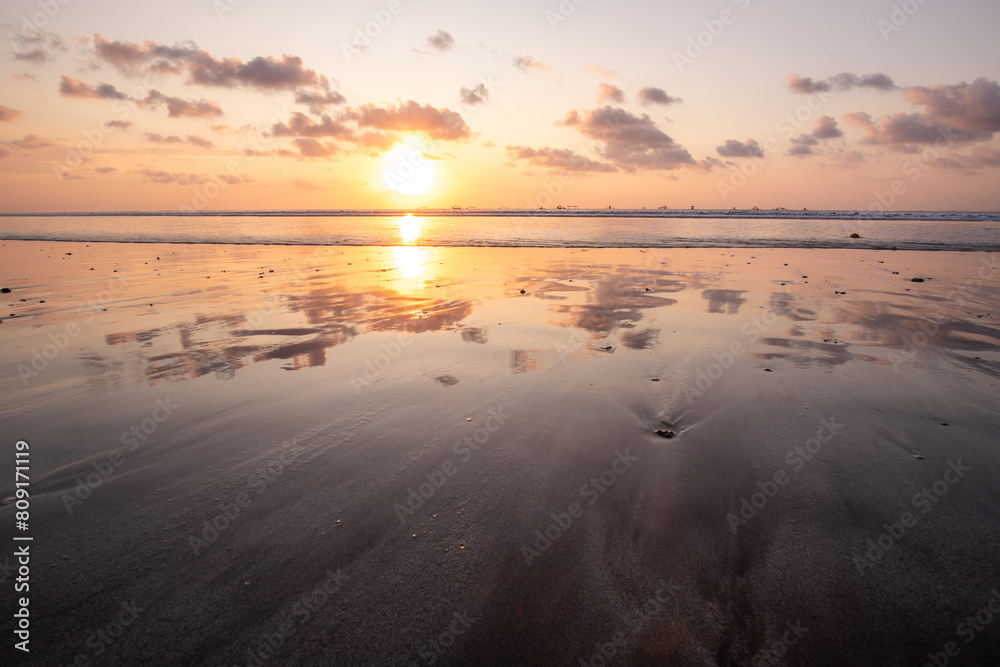Fantastic sunset on the dream beach of Kuta, small waves setting over the sea and the reflection of the sky in the shallow water. News Bali in Indonesia