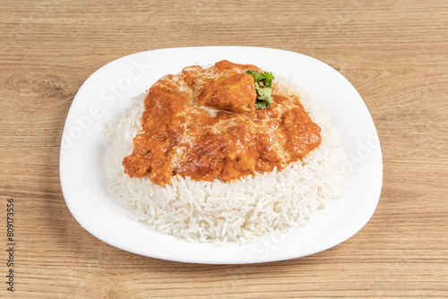A plate of steamed rice with spicy Indian butter chicken on a wooden table