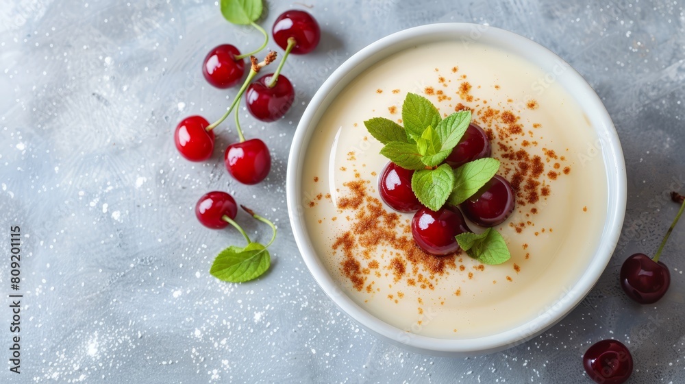 A bowl of yogurt, garnished with cherries and sprinkles, on a gray table Nearby, fresh cherries rest in place A bowl of yogurt, garnished with cherries and sprinkles, on a gray table Nearby, fresh cherries rest in place
