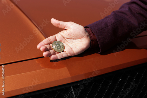 Man holding cryptocurrency golden bitcoin coin against the background of an expensive car