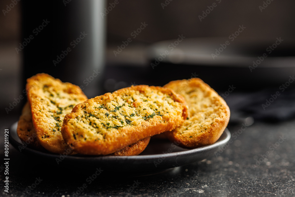 Garlic crisp bread Slices Topped With Herbs onn plate on black table. Garlic crisp bread Slices Topped With Herbs onn plate on black table.
