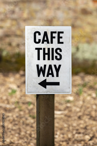 Rustic white wood sign on stake with cafe this way and black arrow pointing way
