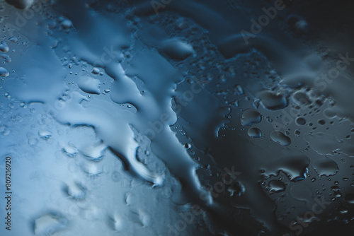 visuale macro di gocce d'acqua di pioggia che cadono e scorrono lungo un vetro in trasparenza in un'atmosfera color blu  photo