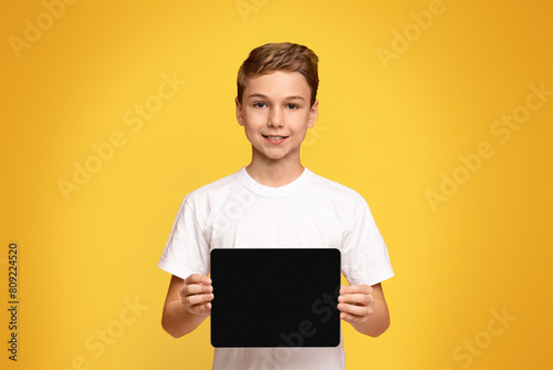 A young boy is holding a black laptop computer in his hands.
