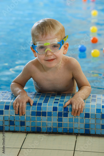Happy cute toddler child near the pool side smiling in goggles after swimming lesson indoor. Physical development and healthy water activities for kids