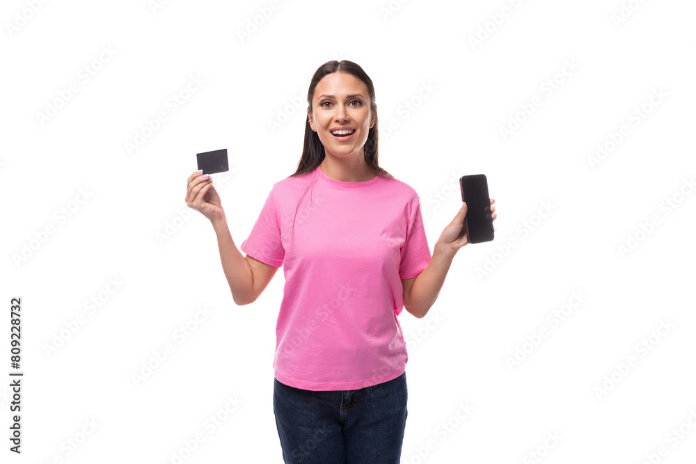 young slim brunette woman in pink basic t-shirt holding credit card mockup and smartphone on white background with copy space young slim brunette woman in pink basic t-shirt holding credit card mockup and smartphone on white background with copy space