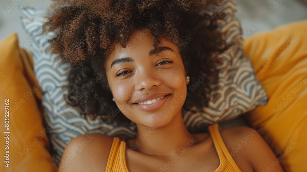 Closeup portrait of beautiful young woman with black afro hairstyle lying on sofa and looking at camera while relaxing in living room Closeup portrait of beautiful young woman with black afro hairstyle lying on sofa and looking at camera while relaxing in living room