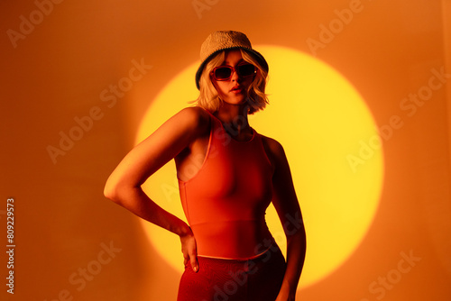 Stylish female model with light natural makeup wearing trendy sunglasses against orange background