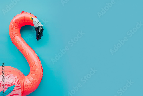 Vibrant pink flamingo inflatable ring positioned against a bright blue backdrop, portraying a minimalist summer vacation and leisure concept, copy space photo
