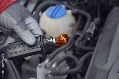 A man holds a car headlight lamp in his hand. Service replacement light bulb