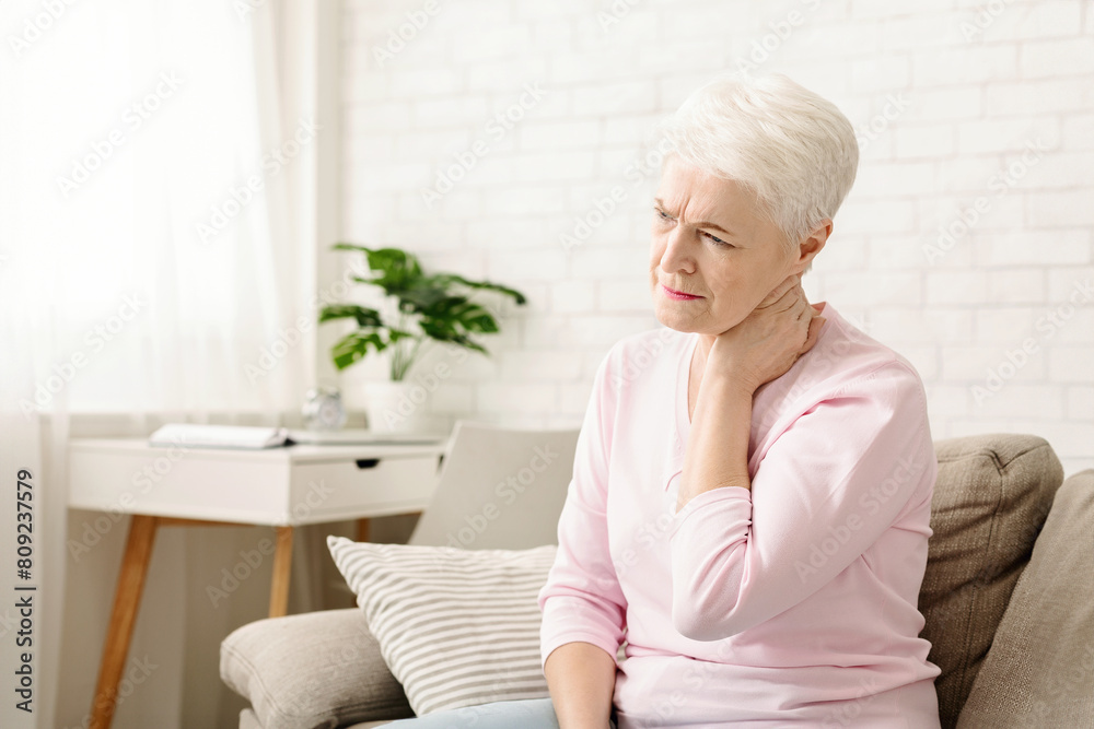 Mature woman suffering from backache at home, massaging neck with hand, feeling exhausted, empty space